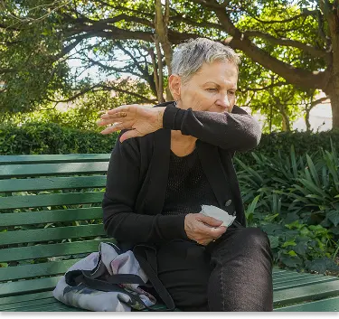 Persona adulta en la banca de un parque, tosiendo.